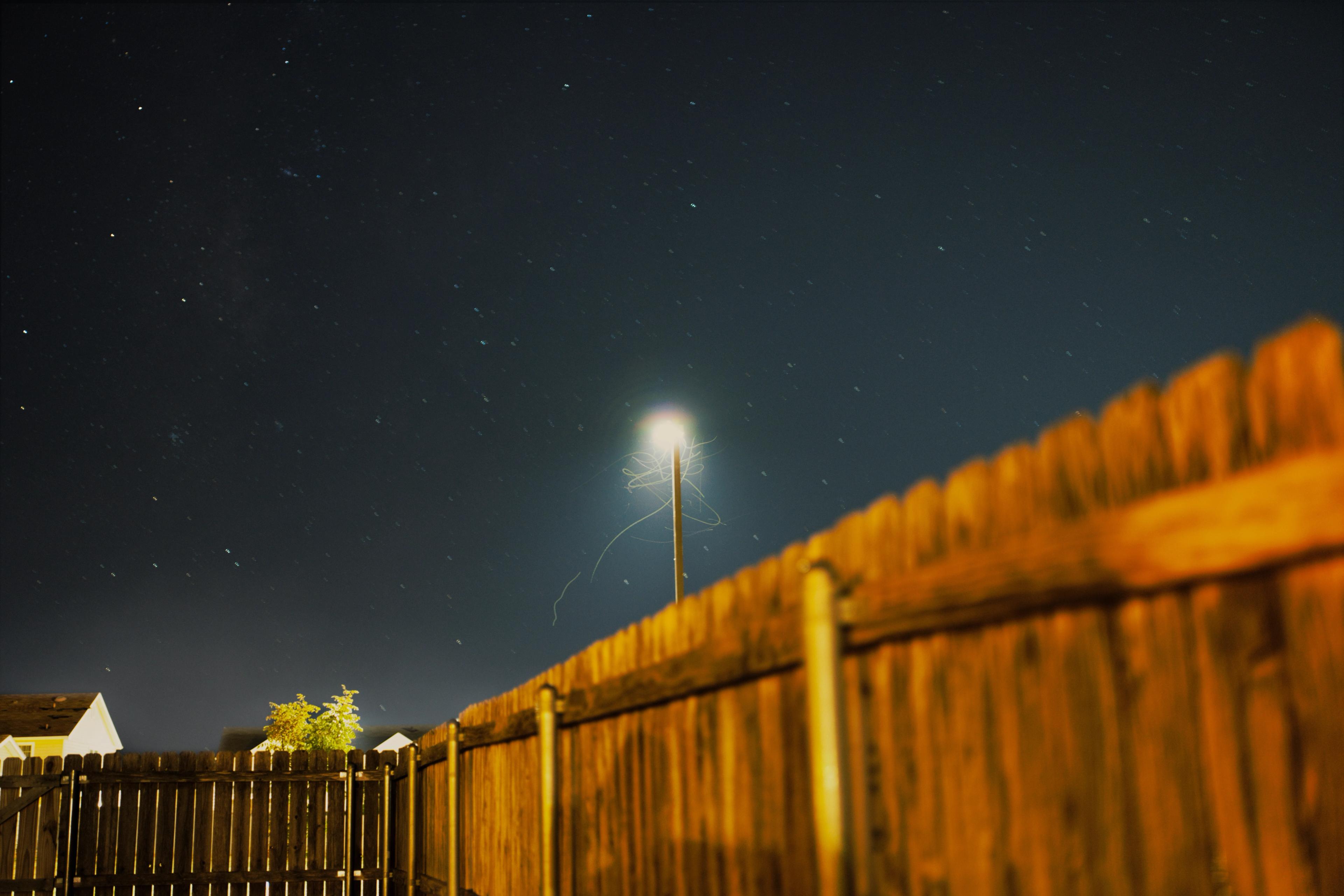 A photo of a street light behind a gate with the night sky in the background